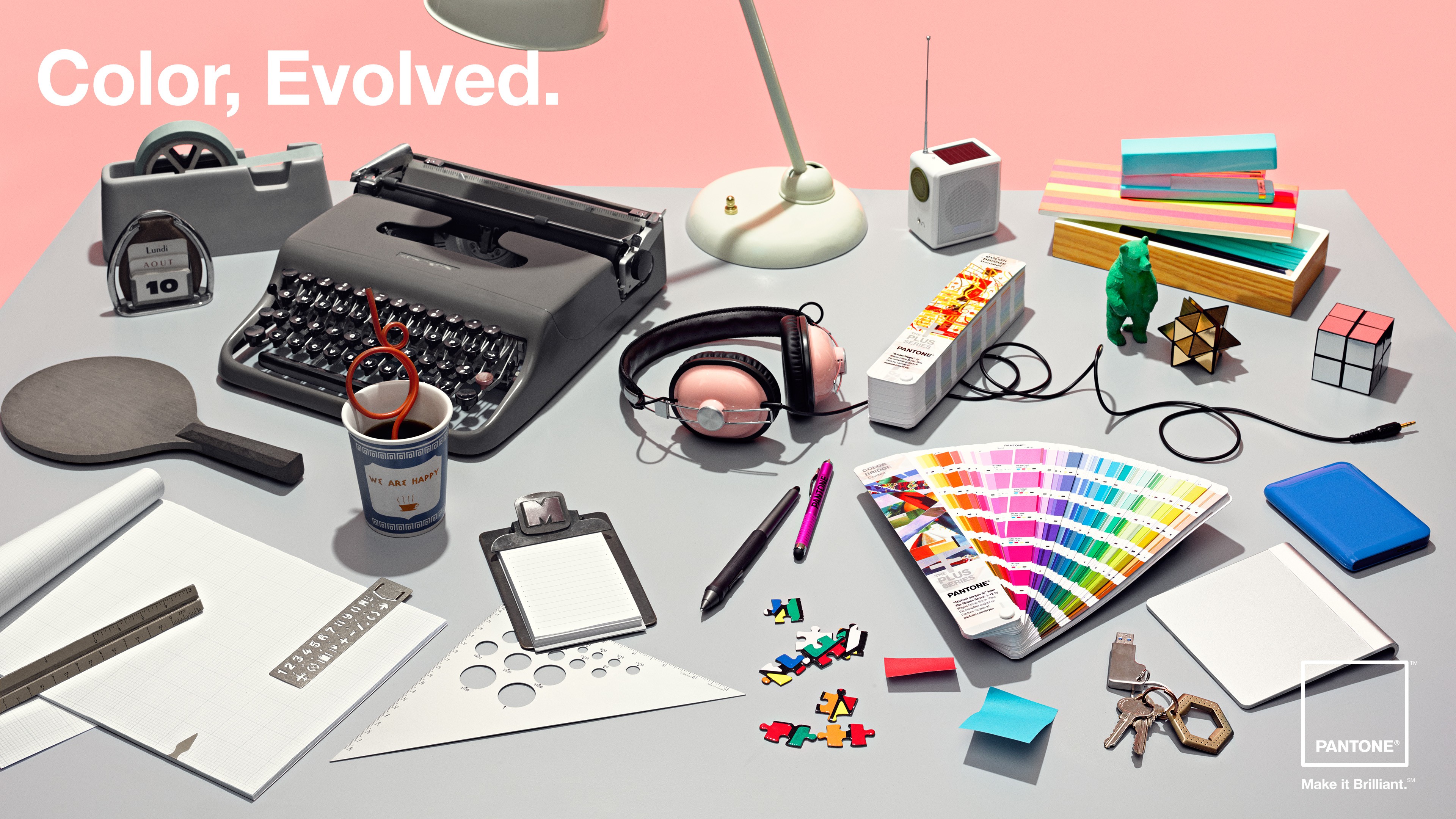 A table with scattered stationary like a typewriter, a colorful colour palette flyer and many other things